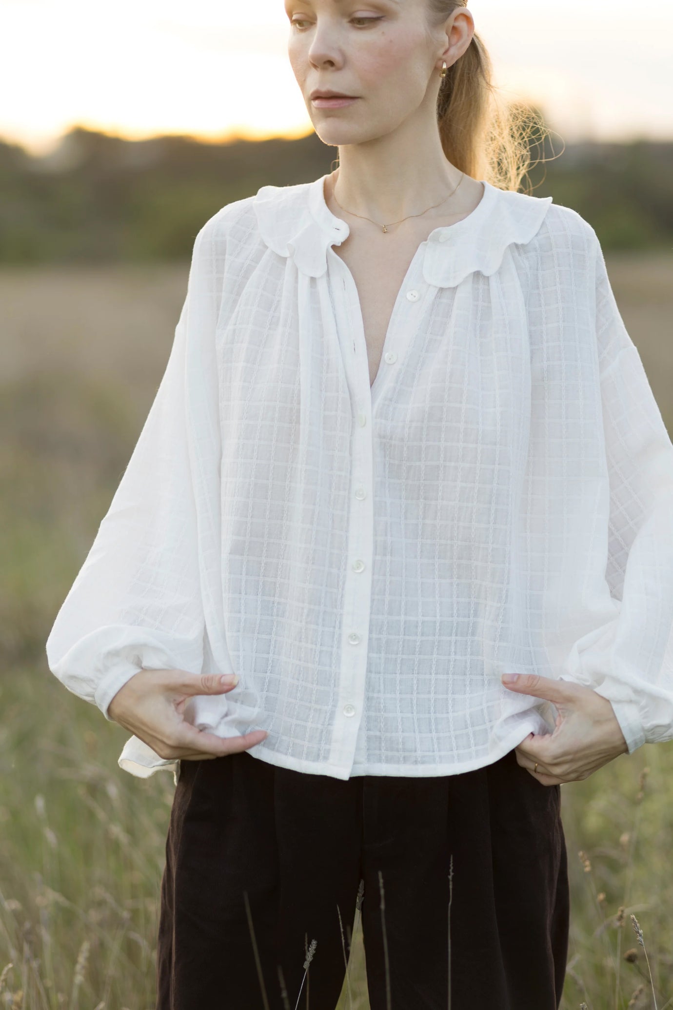 Woman wearing the Amelie Blouse sewing pattern from Silversaga Patterns on The Fold Line. A shirt pattern made in lightweight cotton or lightweight linen fabric, featuring an oversized billowy cut, band collar with a flounce detail, gathered front, button placket, and dropped full-length sleeves with fitted cuffs.