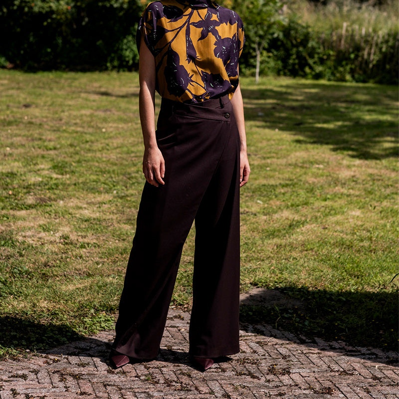 Woman wearing the Bliss Trousers sewing pattern from Fibre Mood on The Fold Line. A trousers pattern made in denim, corduroy,  polycotton, gabardine, flannel, or crepe fabric, featuring an asymmetric wrap front, button closure, back darts, and belt loops.