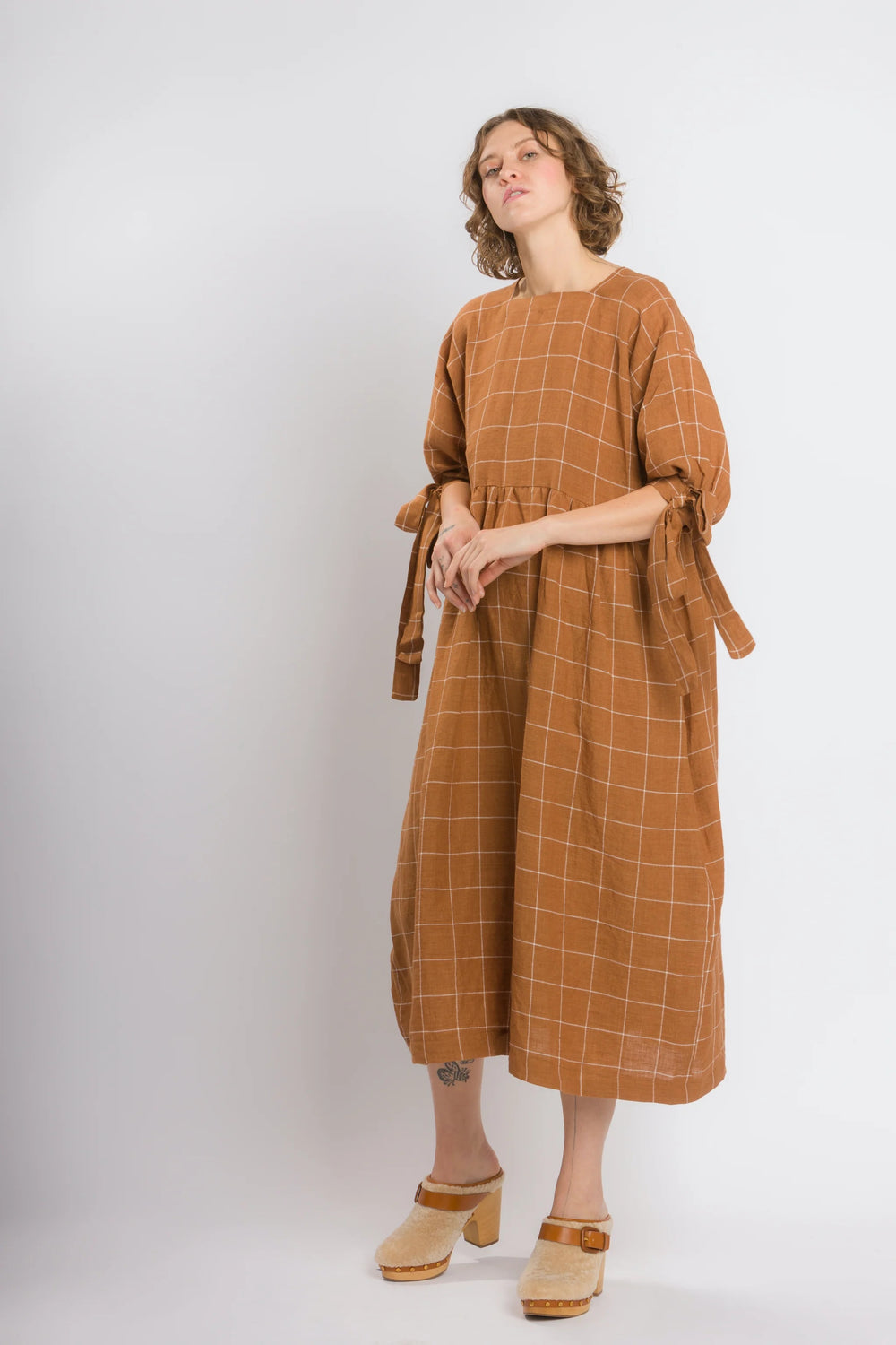 Woman wearing the Daydream Dress sewing pattern from 奥州五开奖官网开奖号 Cris Wood Sews on The Fold Line. A dress pattern made in linen, lightweight cotton, silk, rayon, viscose blend, or gauze fabric, featuring a square neckline, mid-length sleeves with bows, and a midi length.