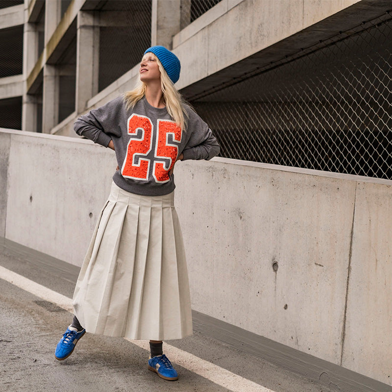 Woman wearing the Fausta Skirt sewing pattern from Fibre Mood on The Fold Line. A pleated skirt pattern made in cotton twill, poplin, viscose (crepe), lyocell, or woollen fabric, featuring a shaped waistband, concealed zip, and midi length.