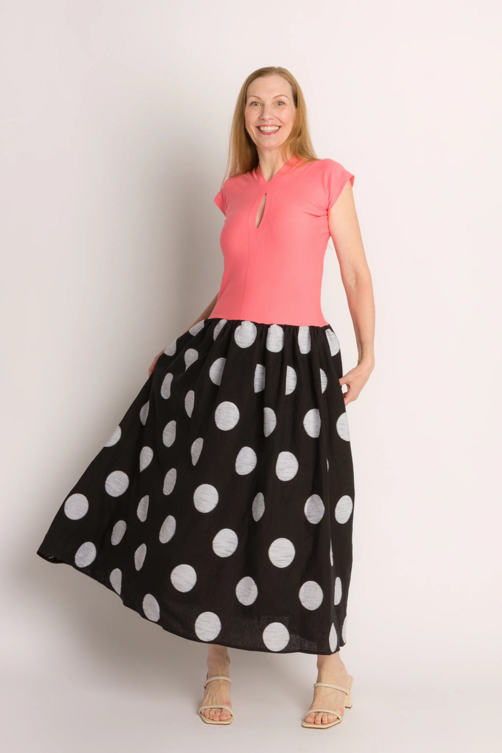 Woman wearing the Harmony Dress sewing pattern from Cris Wood Sews on The Fold Line. A dress pattern made in knit fabric and cotton, linen, viscose, cupro, rayon, or silk fabric, featuring a form-fitting bodice with a high V-neckline and peekaboo opening, grown-on short sleeves, and a full ankle-length skirt with deep pockets.