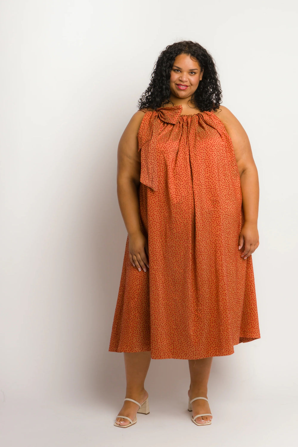 Woman wearing the Juniper Dress sewing pattern from Cris Wood Sews on The Fold Line. A sleeveless dress pattern made in linen, lightweight cotton, silk, rayon, viscose blend, or gauze fabric, featuring an A-line silhouette, gathered neckline, wide straps, and a large bow at the shoulder. 