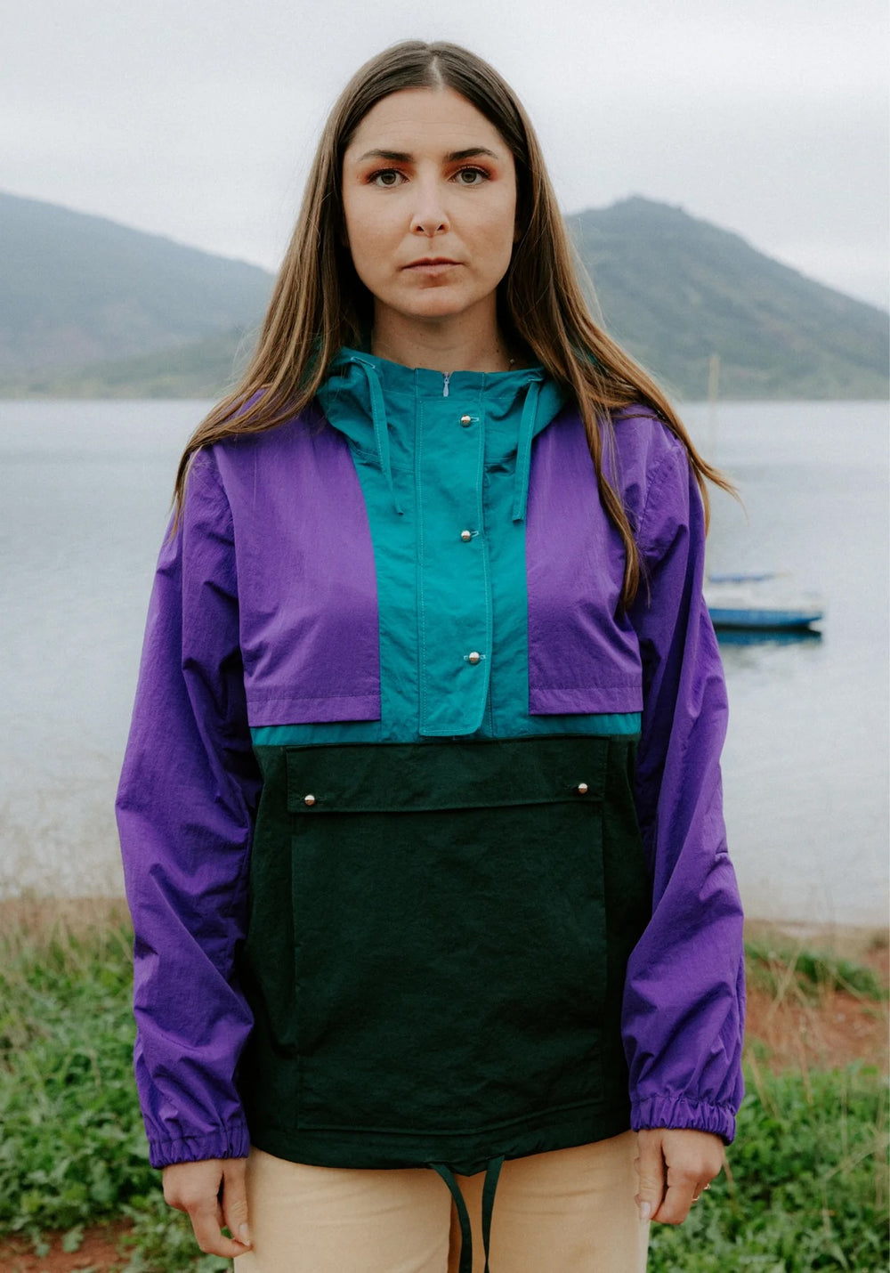 Woman wearing the Rafale Windbreaker sewing pattern from Maison Fauve on The Fold Line. A jacket pattern made in fine denim, coated or water-repellent fabric, gabardine, twill, or cotton satin fabric, featuring colour blocked panels, a large kangaroo pocket with a faux flap, long sleeves with small darts, and a lined hood with a visor and drawstring.