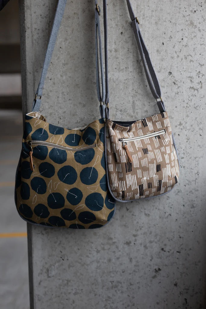 The Trail Tote sewing pattern from Noodlehead on The Fold Line. A crossbody bag pattern made in canvas fabric, featuring a piped edge, exterior zipper pocket, interior slip pocket, adjustable strap, and magnetic closure.