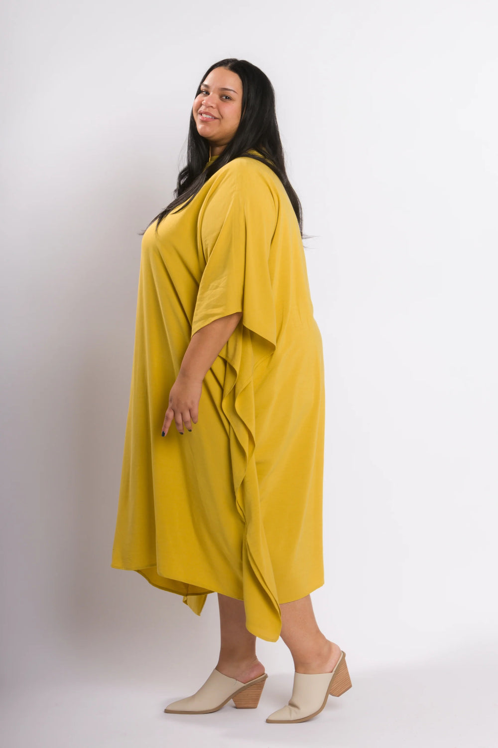 Woman wearing the Waterfall Dress sewing pattern from Cris Wood Sews on The Fold Line. A dress pattern made in linen, lightweight cotton, silk, rayon, viscose blend, or gauze fabric, featuring a slash neckline, wide panels that drape down the sides, and a midi length.